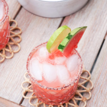 two glasses of watermelon margarita on the rocks with lime wedges