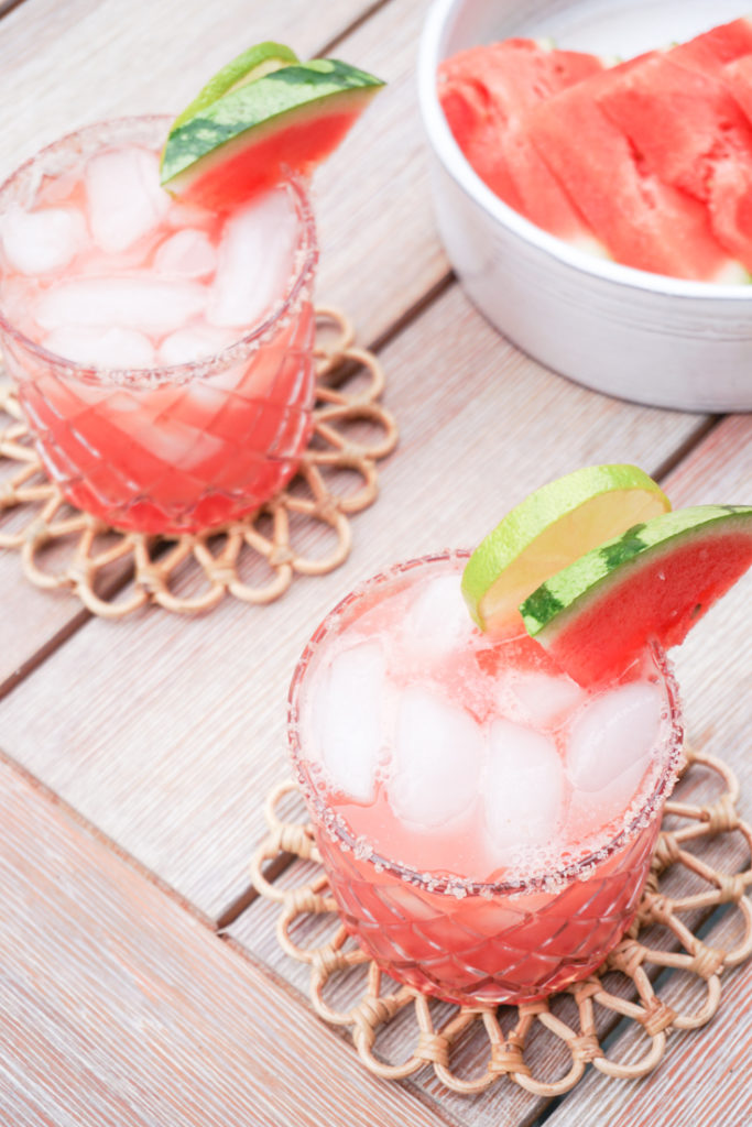two glasses of watermelon margarita on the rocks with lime wedges