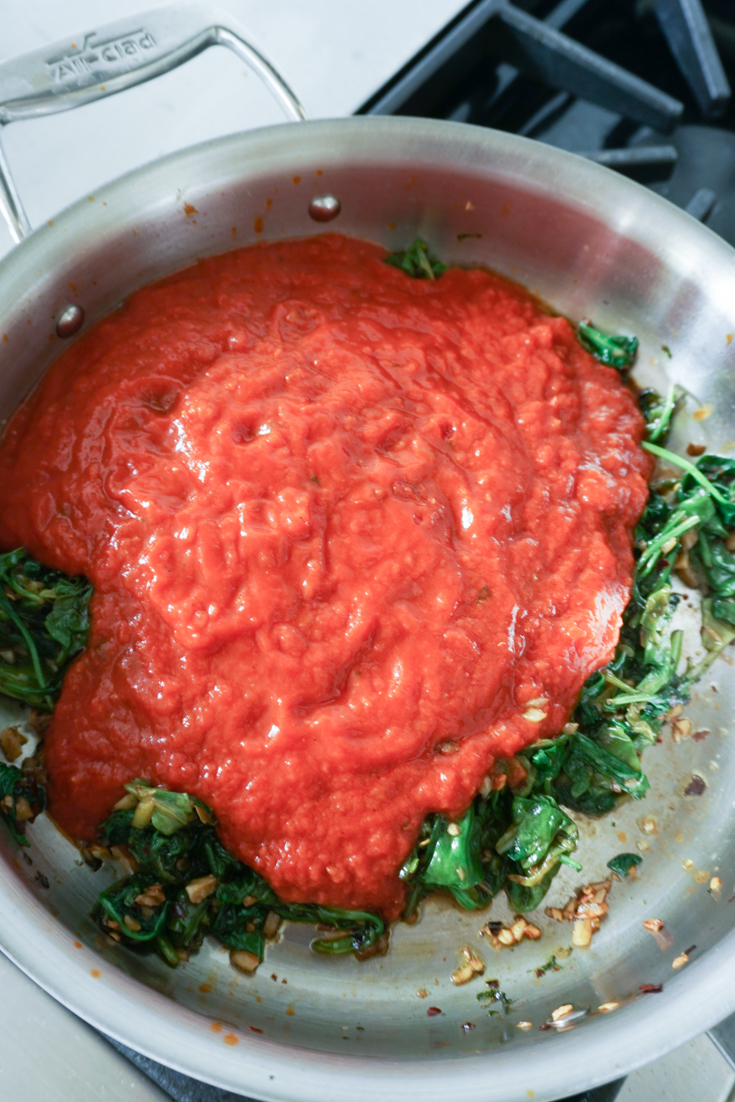 Marinara sauce over wilted spinach in a pan