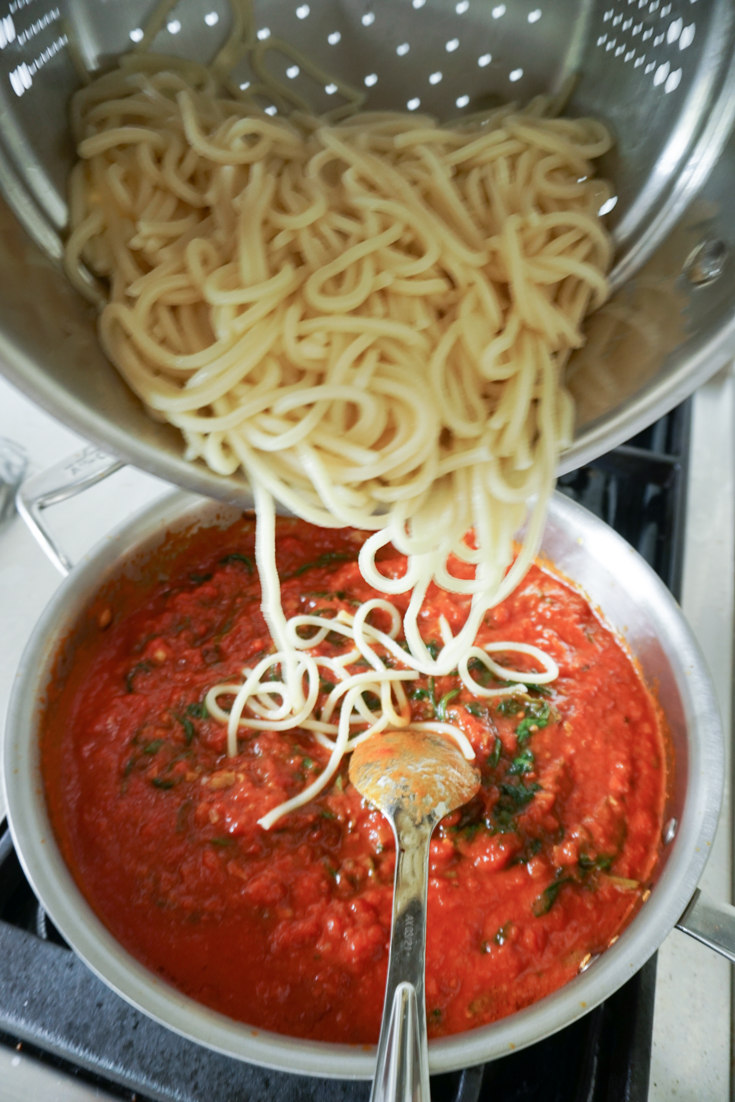 spaghetti being added to a pan with sauce