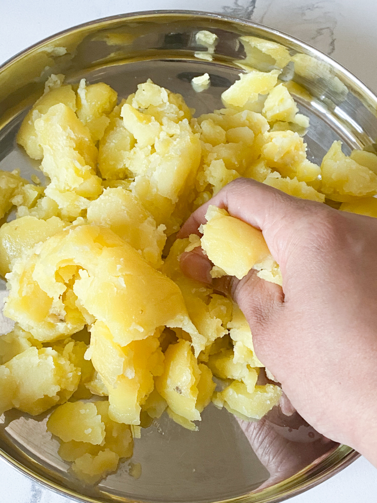 hand crumbling potatoes in a stainless steel plate