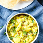 potato curry in a bowl and three pooris in a plate