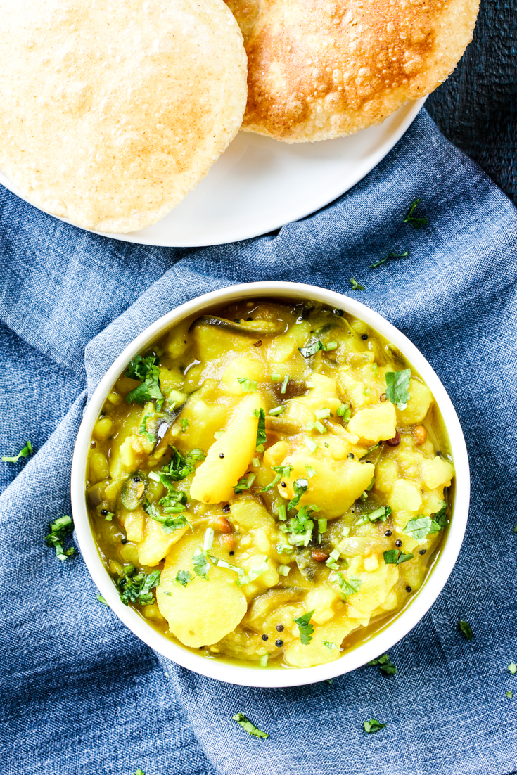 potato curry in a bowl and three pooris in a plate