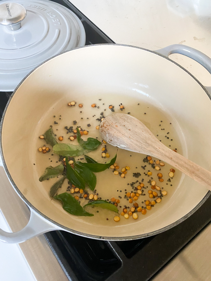 curry leaves and mustard seeds in an enameled cast iron pot with a wooden spoon in it