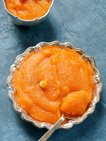 Rava kesari in a silver bowl with a silver spoon in it