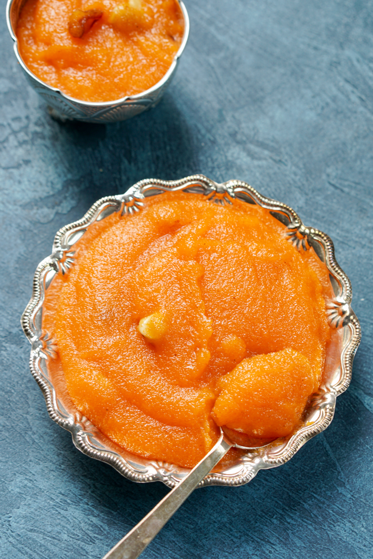 Rava kesari in a silver bowl with a silver spoon in it