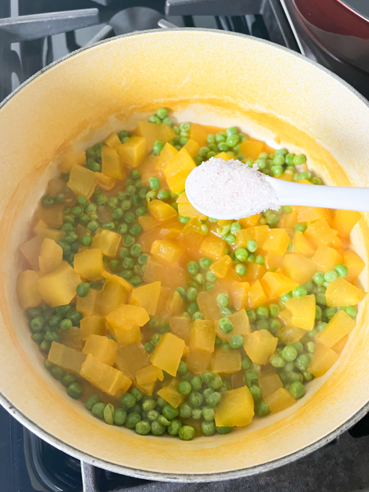 salt being added to pot with cooked pumpkin and green peas