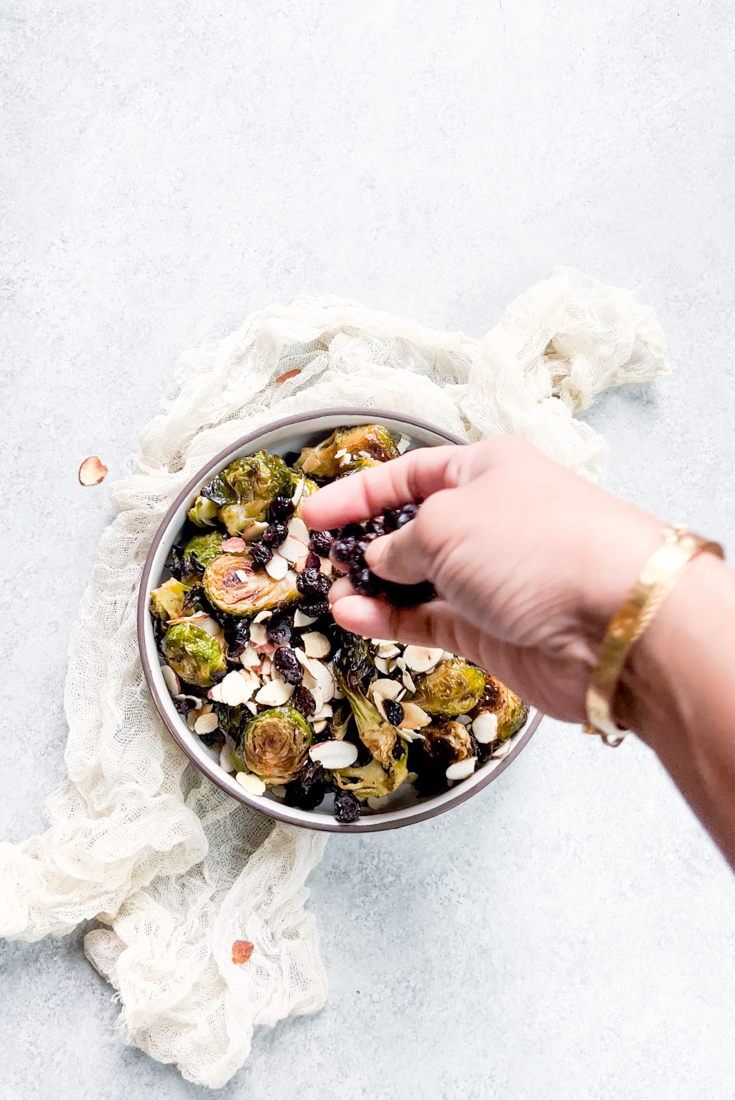 hand sprinkling dried cranberries on to the bowl of brussels sprouts