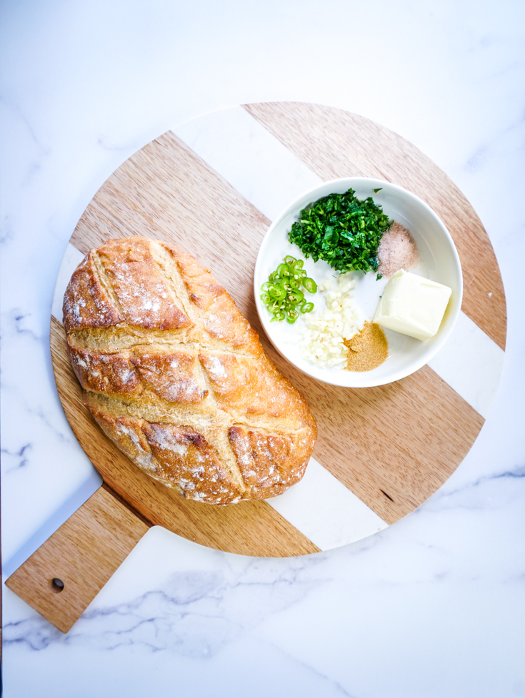 Italian bread and a bowl of butter and herbs on a wooden board