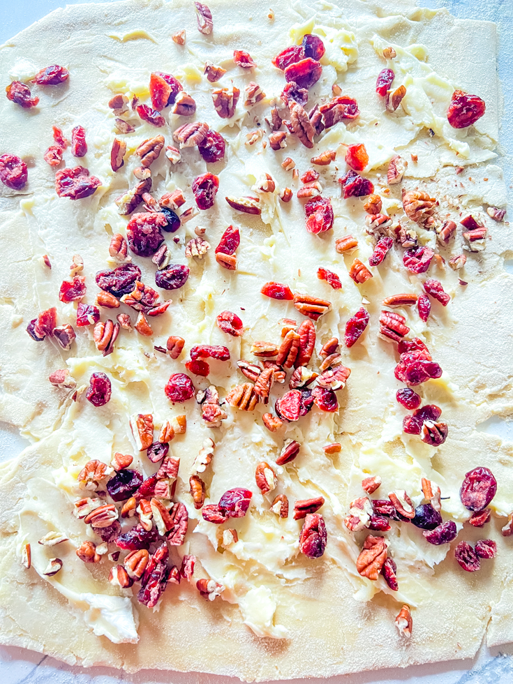 puff pastry sheet with brie, dried cranberries and pecans on it