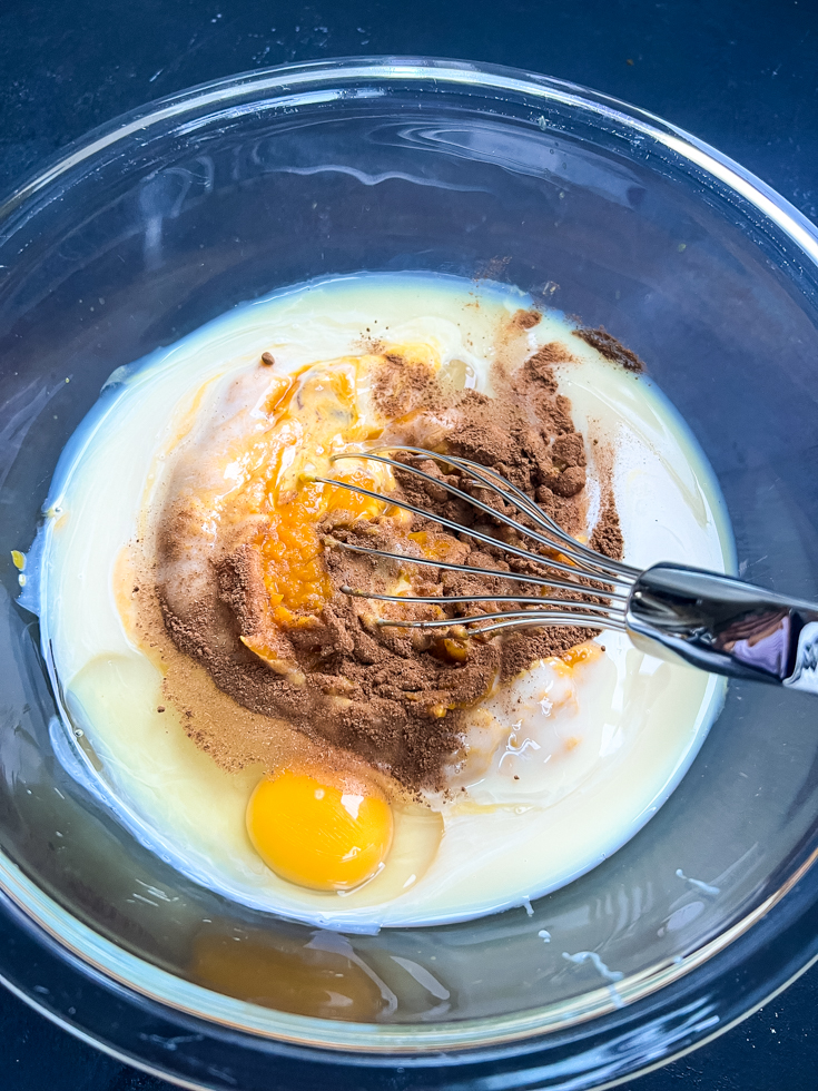 ingredients for pumpkin custard all ready to be whisked in a glass bowl