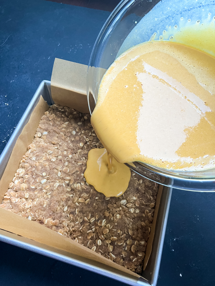 pumpkin custard being poured over shortbread crust in a square baking pan