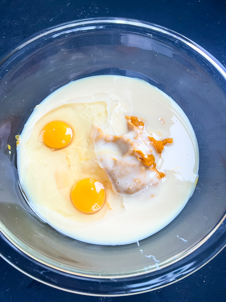 ingredients for pumpkin custard being added to a glass mixing bowl