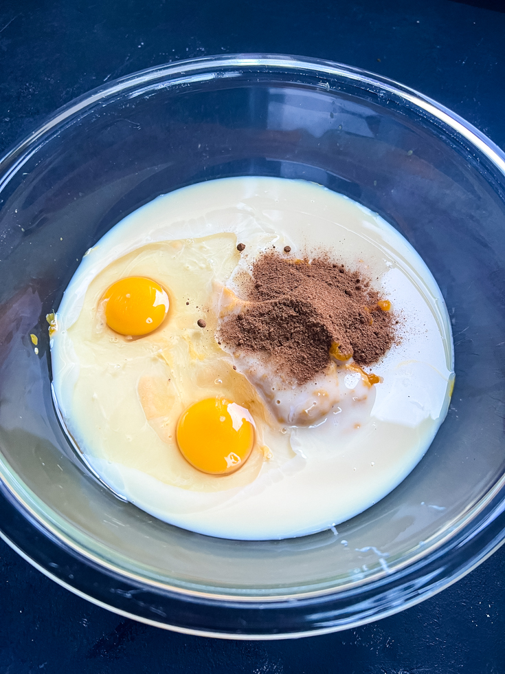 ingredients for pumpkin custard being added to a glass mixing bowl