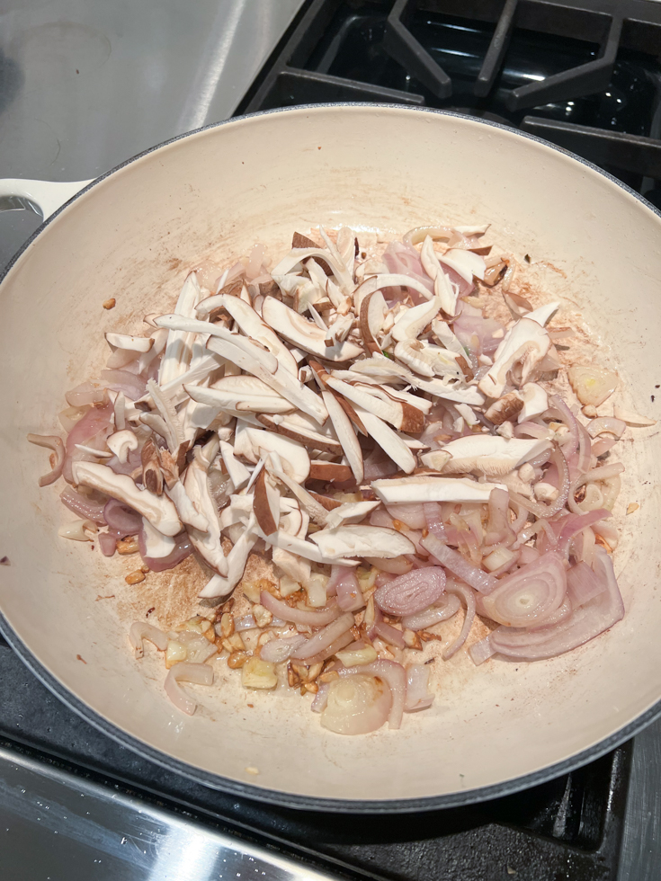 mushrooms added to a pan with sautéed onions in it