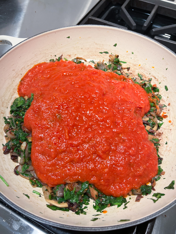 marinara sauce atop the mushroom and spinach mixture in a pan