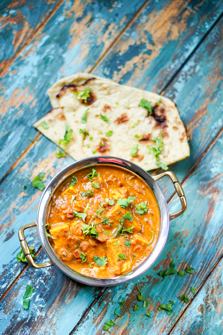 paneer masala in a copper and steel kadhai with a piece of naan on the side