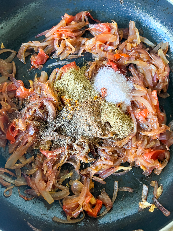 spice powders on top of onion and tomatoes in a pan