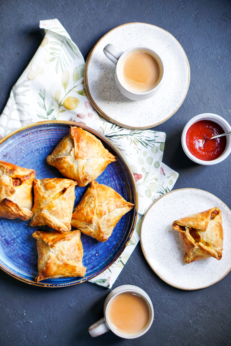 a blue plate of egg puffs and two cups of chai on the side