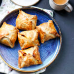 a blue plate of egg puffs and a cup of chai on the side