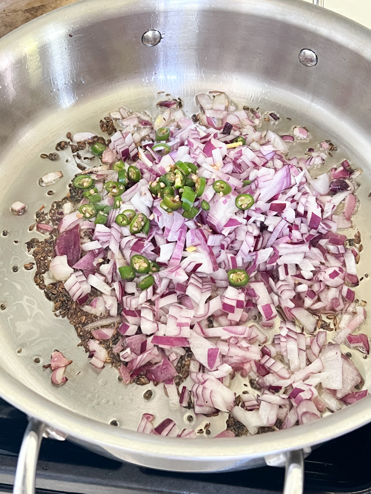 chopped red onions and green chillies in a stainless steel pan
