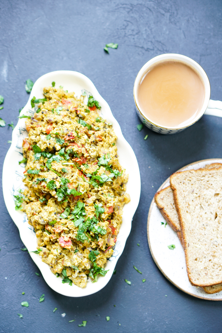 egg bhurji in a white oval platter with a cup of chai and a plate of toast next to it