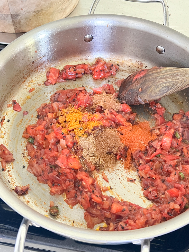 spice powders added to sautéed onion tomato mixture in a stainless steel pan