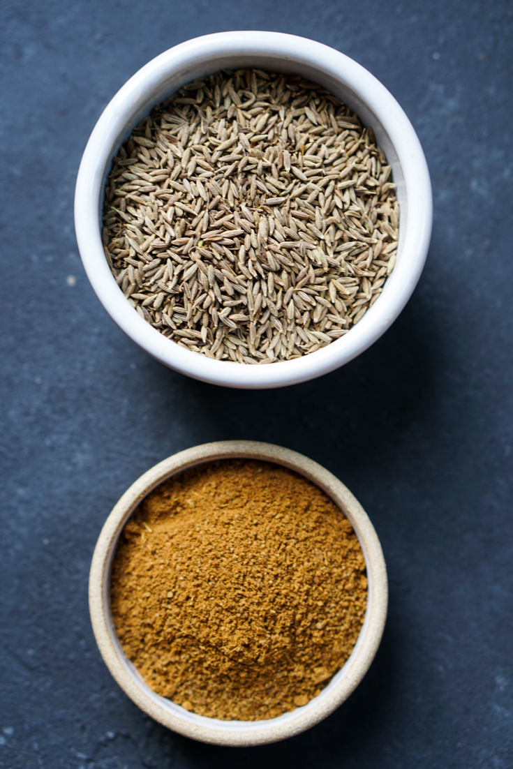 A bowl of cumin seeds alongside a smaller bowl of cumin powder