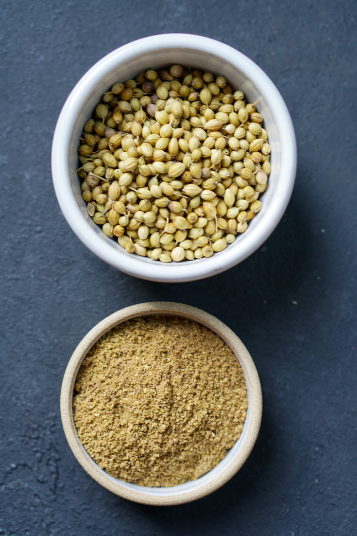 A bowl of coriander seeds alongside a smaller bowl of coriander powder