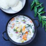 Stew with potato, carrot and green beans in coconut milk in a black kadai bowl and a bowl of idlis