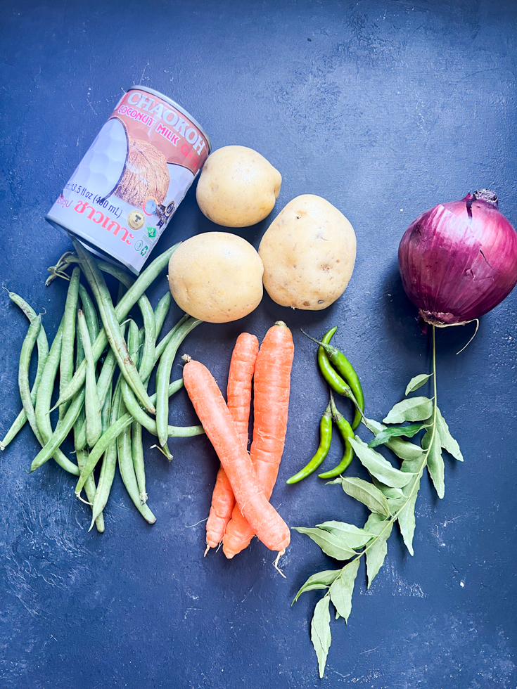 Ingredients for the stew laid out - can of coconut milk, potatoes, green beans, carrots, green chillies, curry leaves, red onion