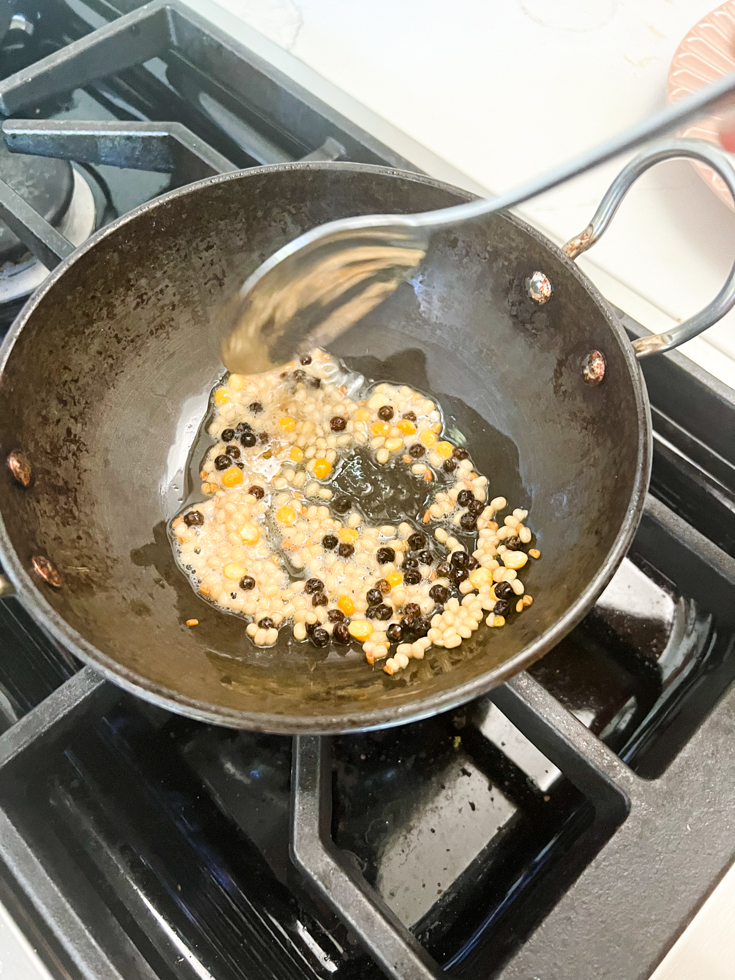 lentils and peppercorns being roasted in oil in a black pan