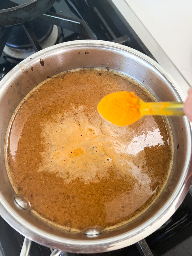 turmeric powder being added to the saucepan with tamarind water in it