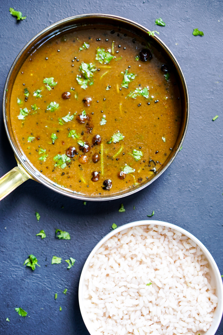 a pan with brass handle with vathal kuzhambu curry in it and a small bowl of rice next to it