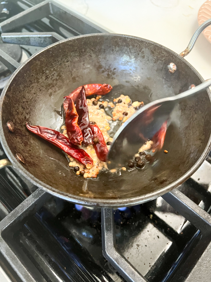 spoon stirring lentils and chillies in a black pan