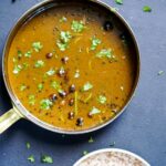 a pan with brass handle with vathal kuzhambu curry in it and a bowl of rice next to it