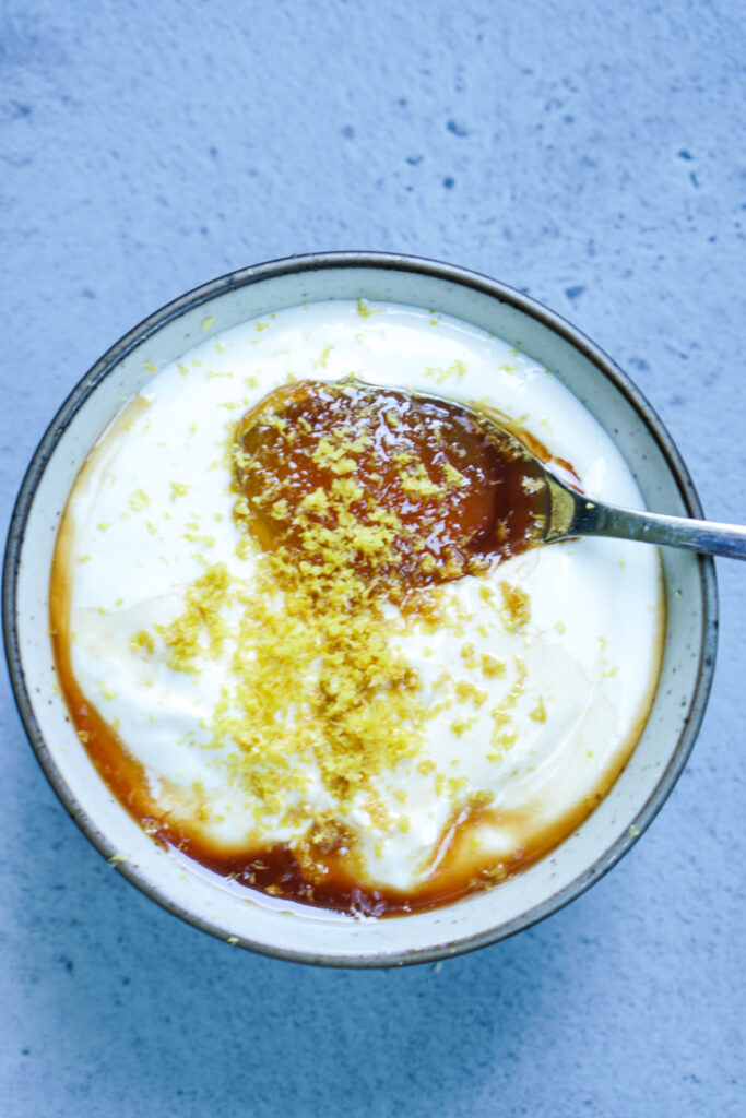 yogurt, honey, vanilla and lemon zest in a bowl with a spoon in it