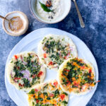 A set of four veggie uthappams in a plate with a bowl of chutney next to it