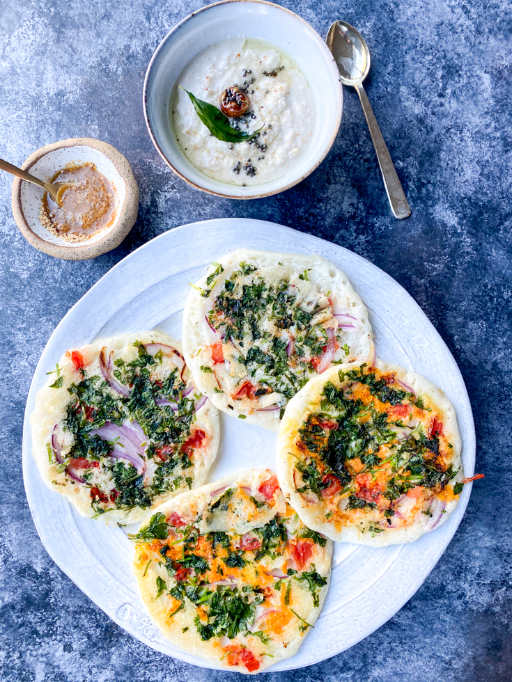 A set of four veggie uthappams in a plate with a bowl of chutney next to it