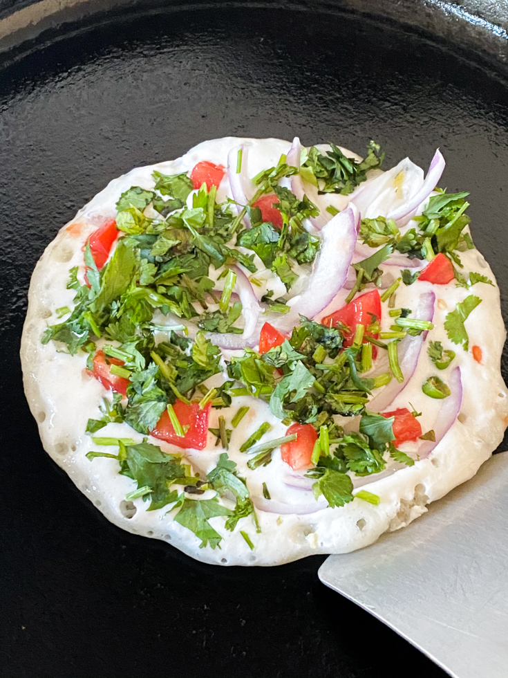 a flat spatula lifting up the uthappam from the griddle