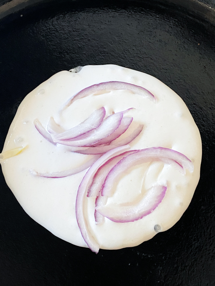 red onion slices on uthappam batter in a pan