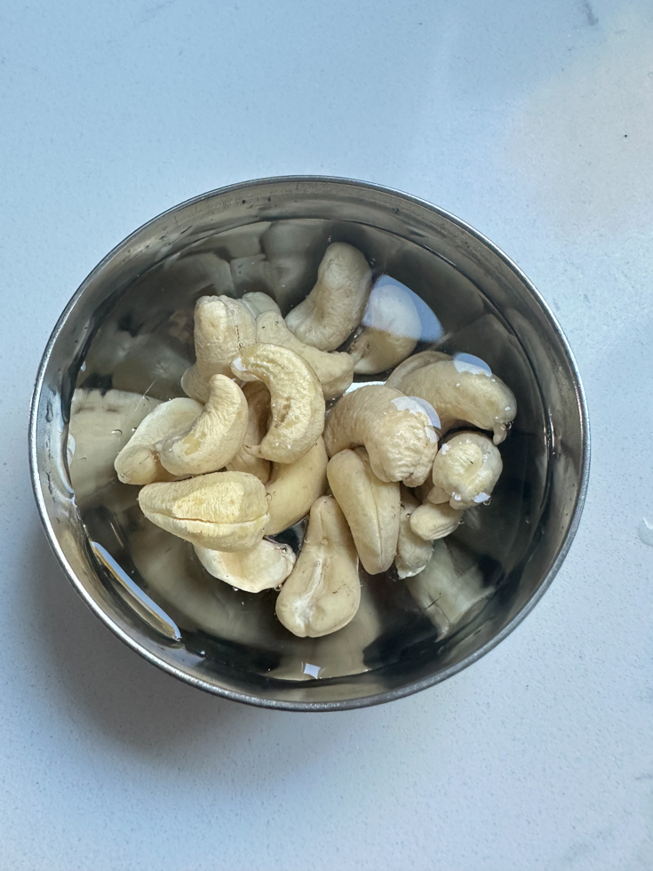 cashews soaking in water in a small stainless steel bowl