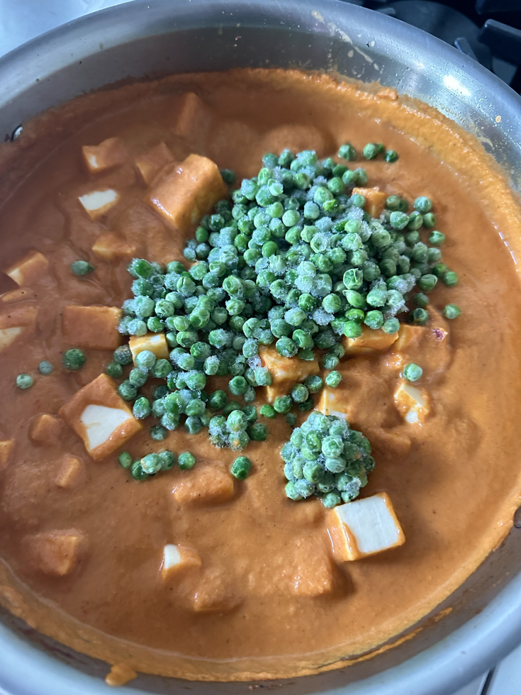 frozen green peas added to the paneer and tomato sauce in a pan
