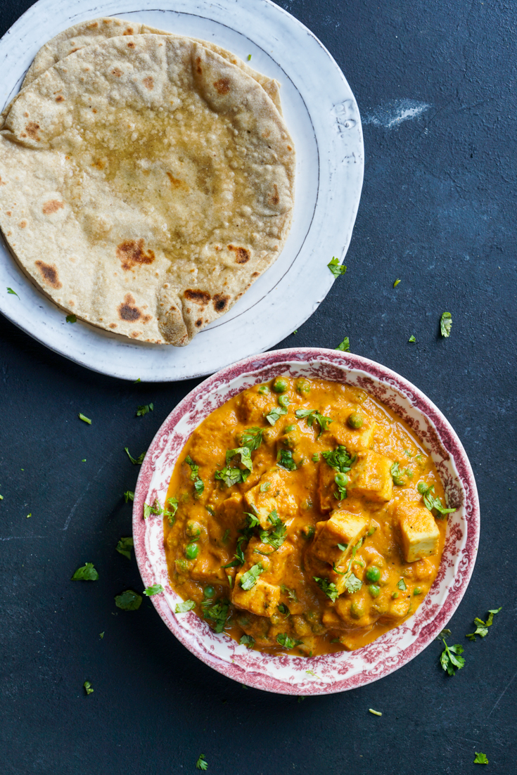 matar paneer in a red and white bowl and a white plate with rotis on it