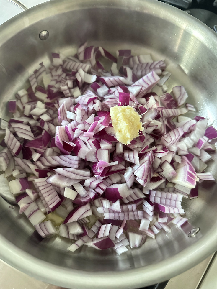 ginger and garlic paste on top of chopped red onions in a pan