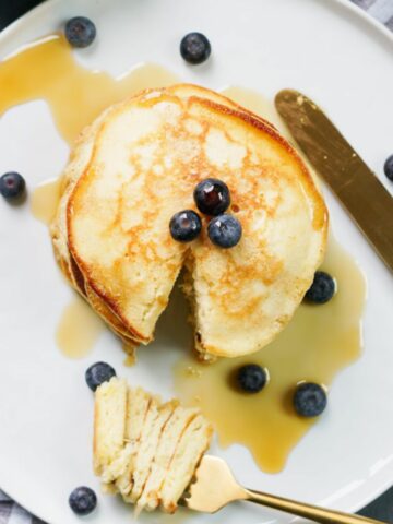 a bite of pancake on a fork on a white plate with a pancake stack on it