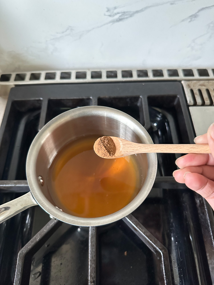ground cinnamon being added to a sauce pan with apple cider in it