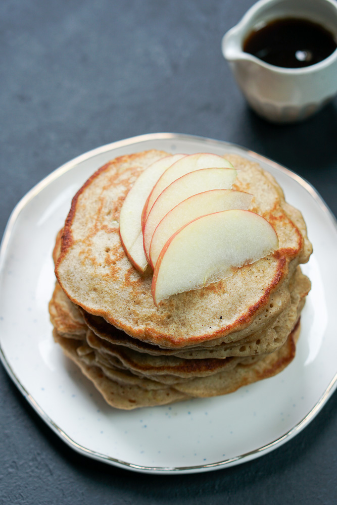 A stack of pancakes with sliced apples on top of it