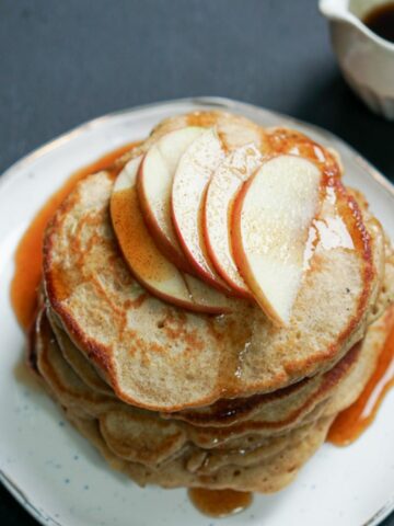 A stack of pancakes with sliced apples and syrup on top